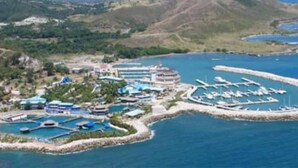Vue aérienne d’une station balnéaire dotée de plusieurs piscines, d’un port de plaisance et bordée de montagnes.