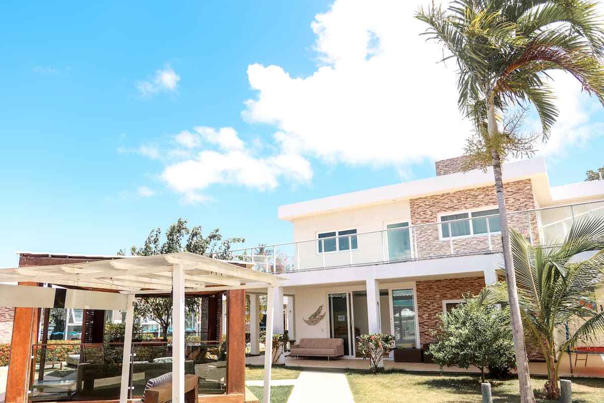 Una casa moderna de dos pisos con un porche cubierto, césped y una palmera.