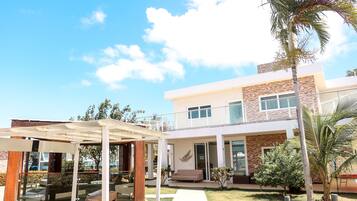 A modern two-story house with a covered patio, a lawn, and a palm tree.