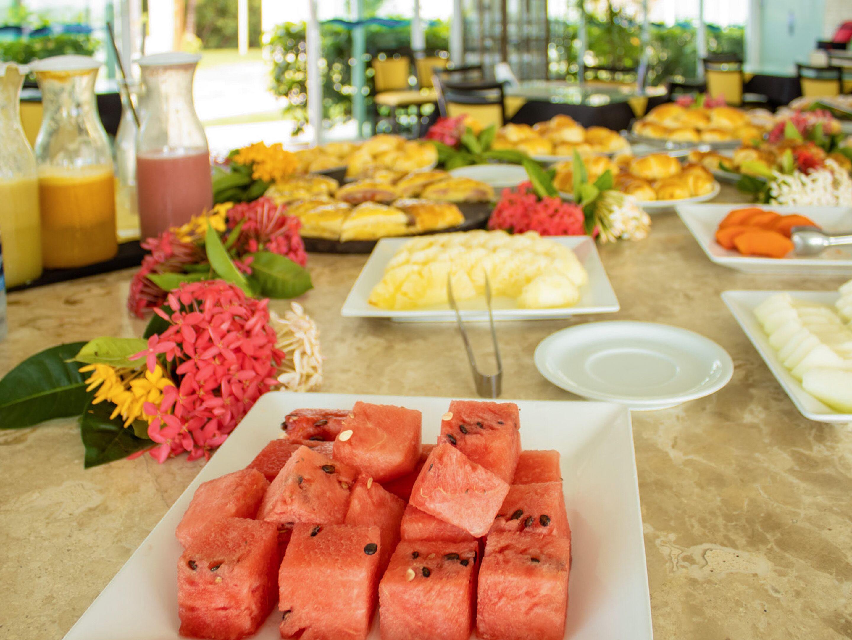Una mesa de buffet con diversas opciones de comida, incluyendo sandía, frutas y pasteles.