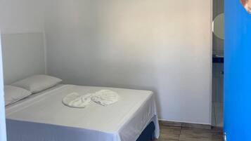 A hotel room with a bed, white linens, a wall-mounted air conditioner, and a wooden floor.