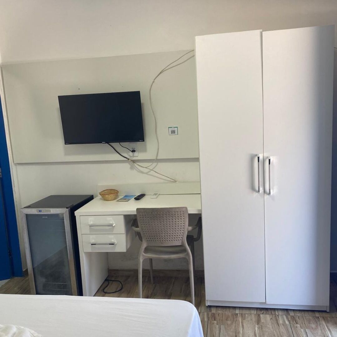 A room with a bed, a desk with a computer, a television mounted on the wall, and a wardrobe.