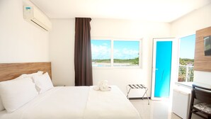 A hotel room with a bed, a desk, a chair, a window with a view, and a door. - Pousada Jirituba (Barra de Santo Antonio)