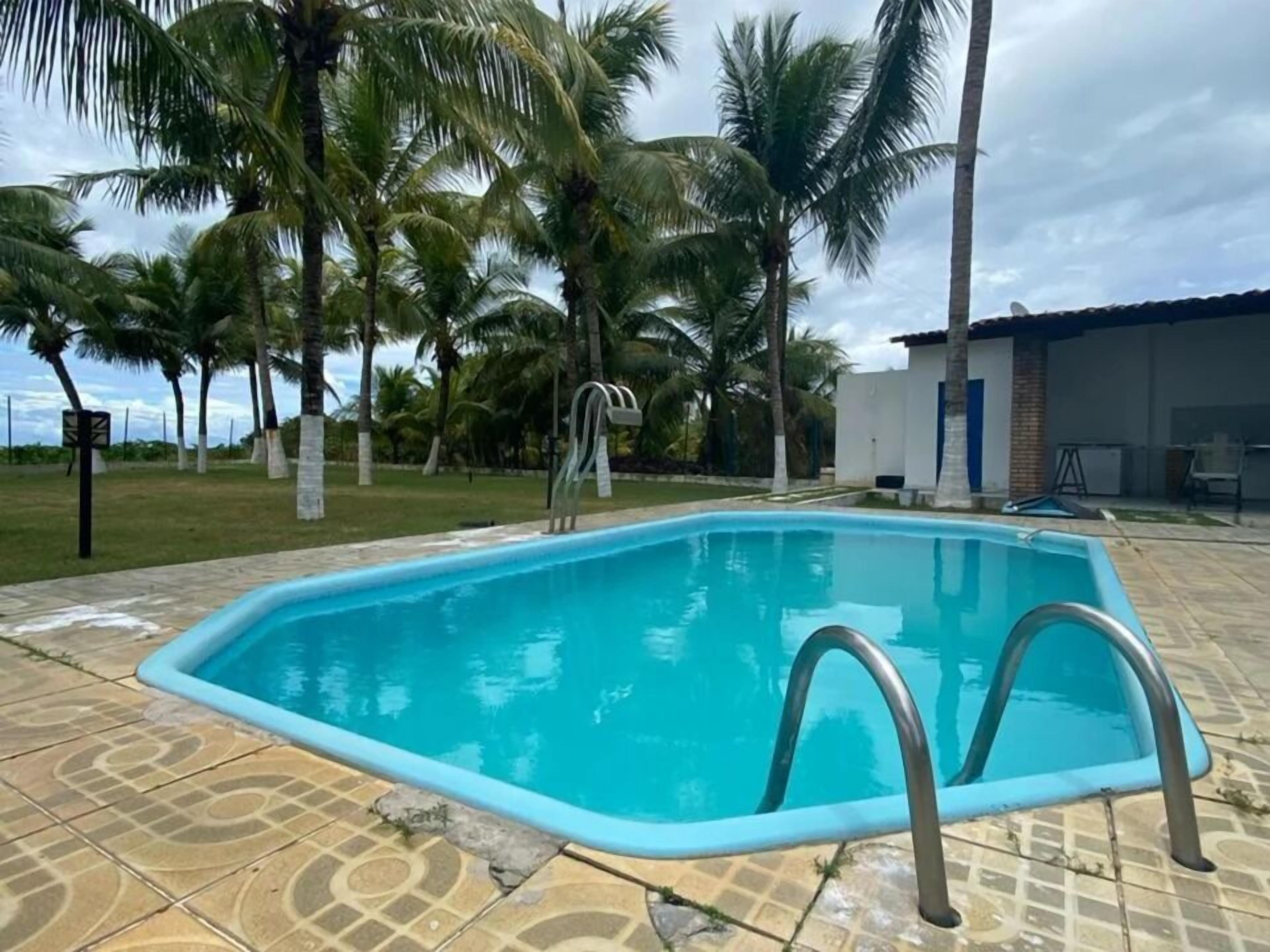 A swimming pool with a tiled deck, surrounded by palm trees and a building with a tiled roof.