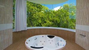 A circular hot tub with a wooden floor, surrounded by wooden walls, and a view of green trees through a large window. - Pousada Jirituba (Barra de Santo Antonio)
