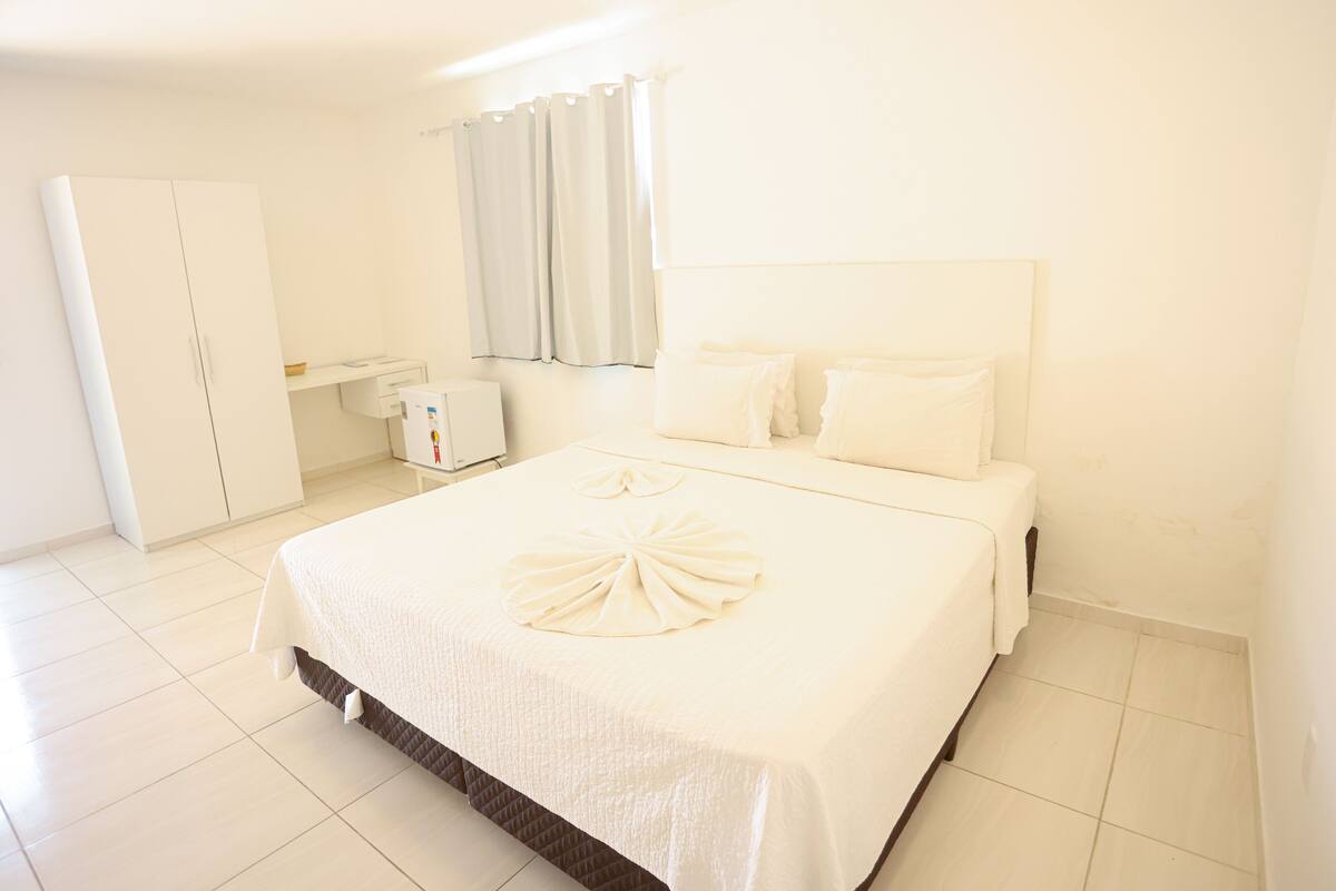 Habitación de hotel con una cama grande, un armario, un escritorio y una ventana con cortinas.
