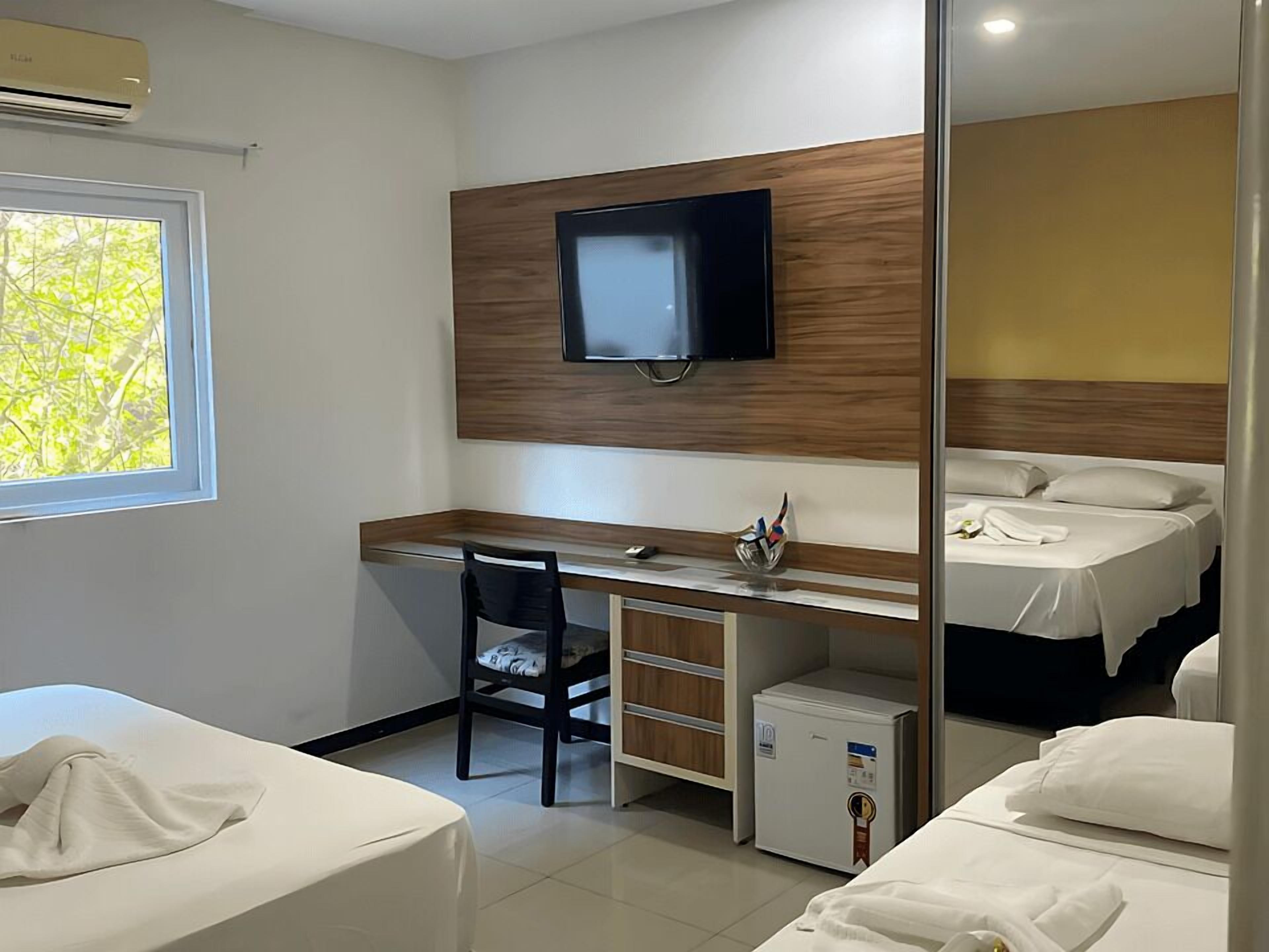A hotel room with a bed, a desk with a chair, a television, and a small refrigerator.