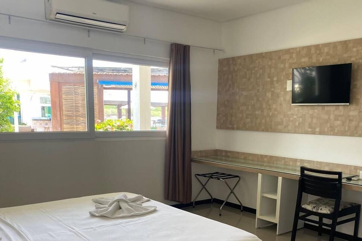 Habitación de hotel con cama, escritorio, silla, televisor de pantalla plana y aire acondicionado.