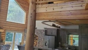 Una cabaña espaciosa con techo alto, un balcón de madera, una zona de cocina y un área de estar con un sofá rojo.