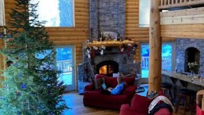 Interior de una cabaña de madera con chimenea de piedra, sofás rojos y un árbol de Navidad decorado.