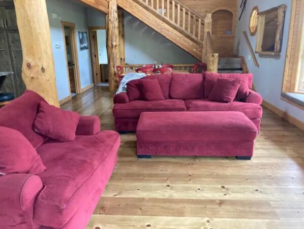 Amplia sala de estar con una escalera de madera, un sofá rojo y piso de madera.