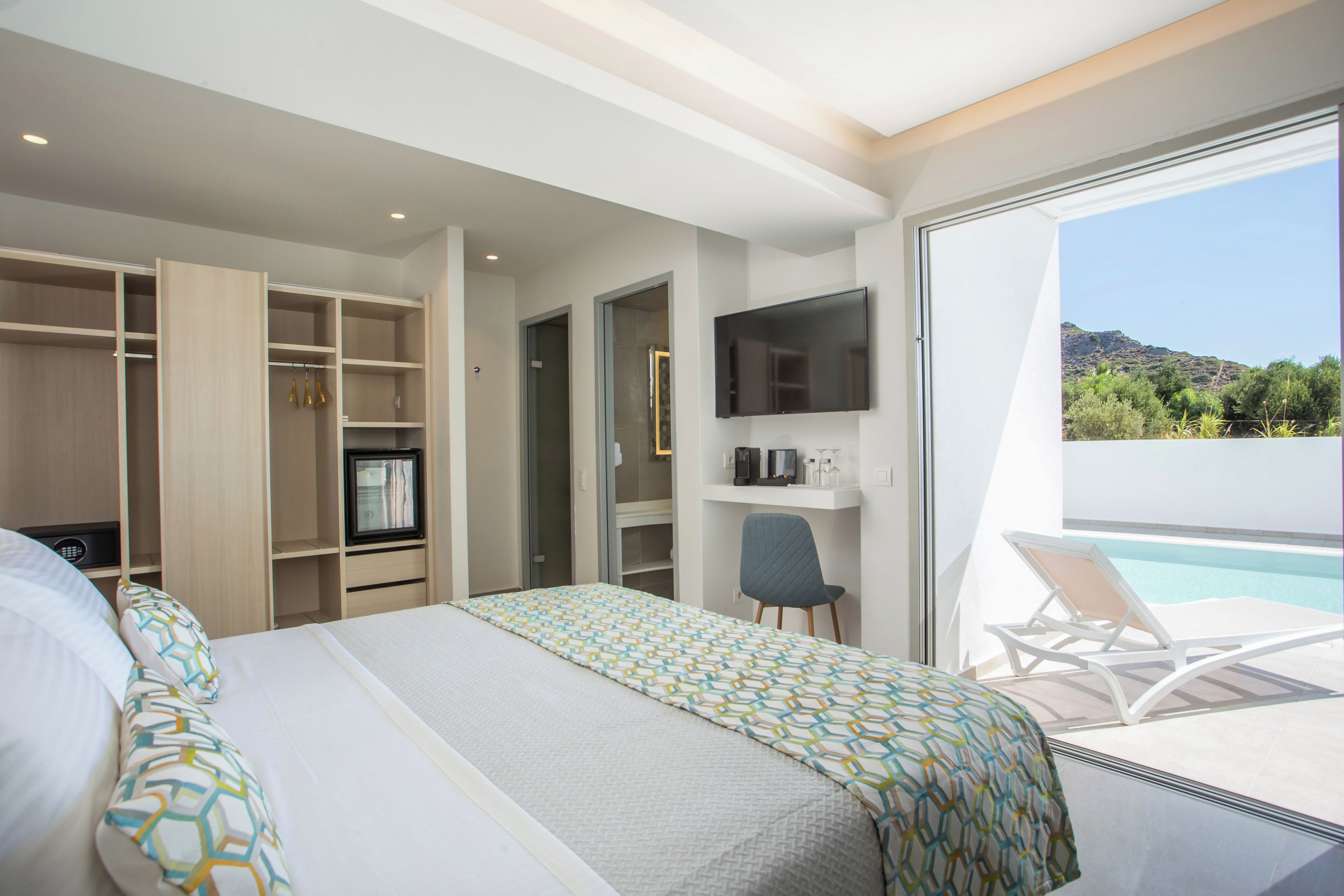 Habitación de hotel con cama, escritorio, televisión y vistas a una piscina y montañas.