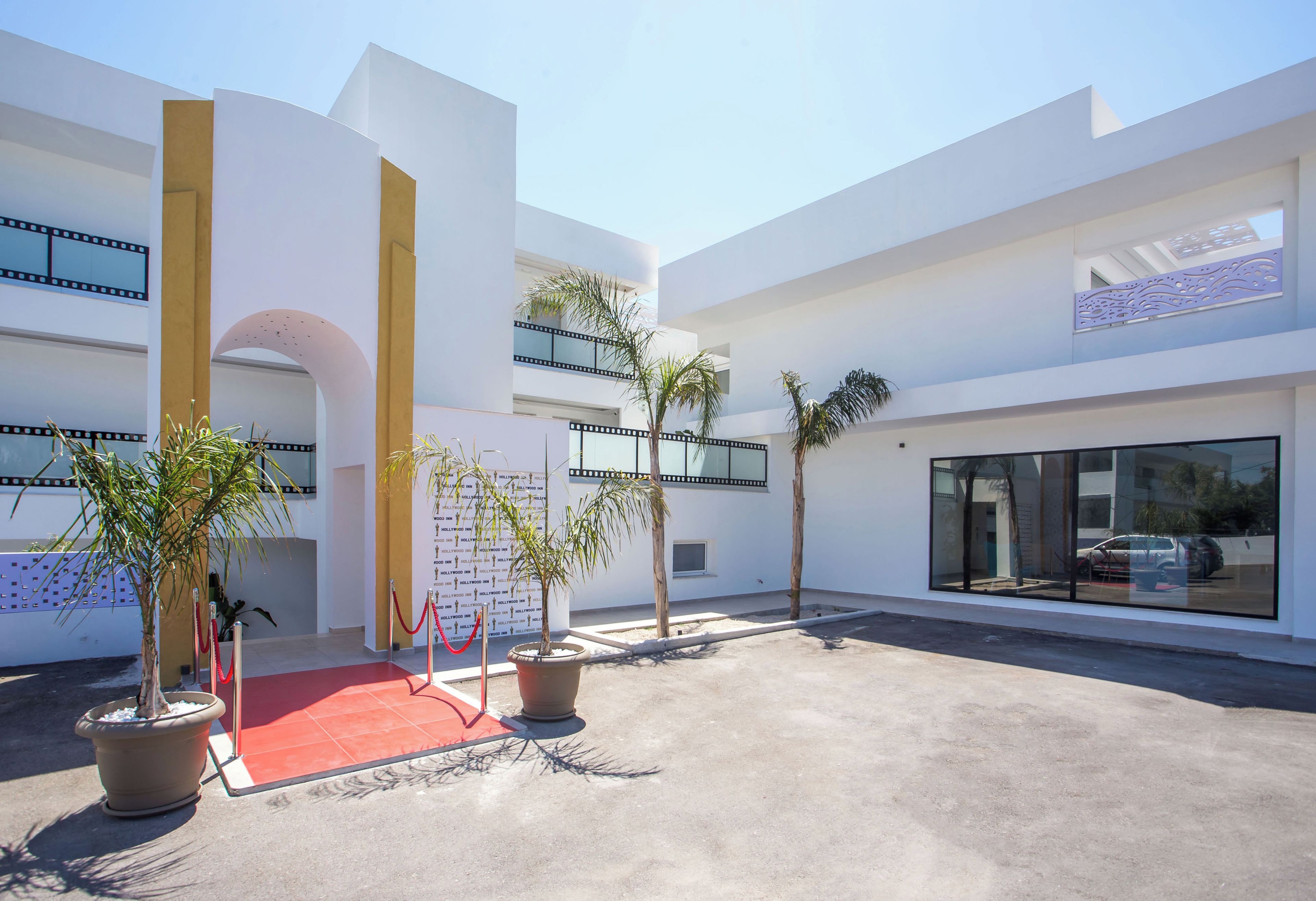 Un edificio moderno con alfombra roja, plantas en macetas y cielo despejado.