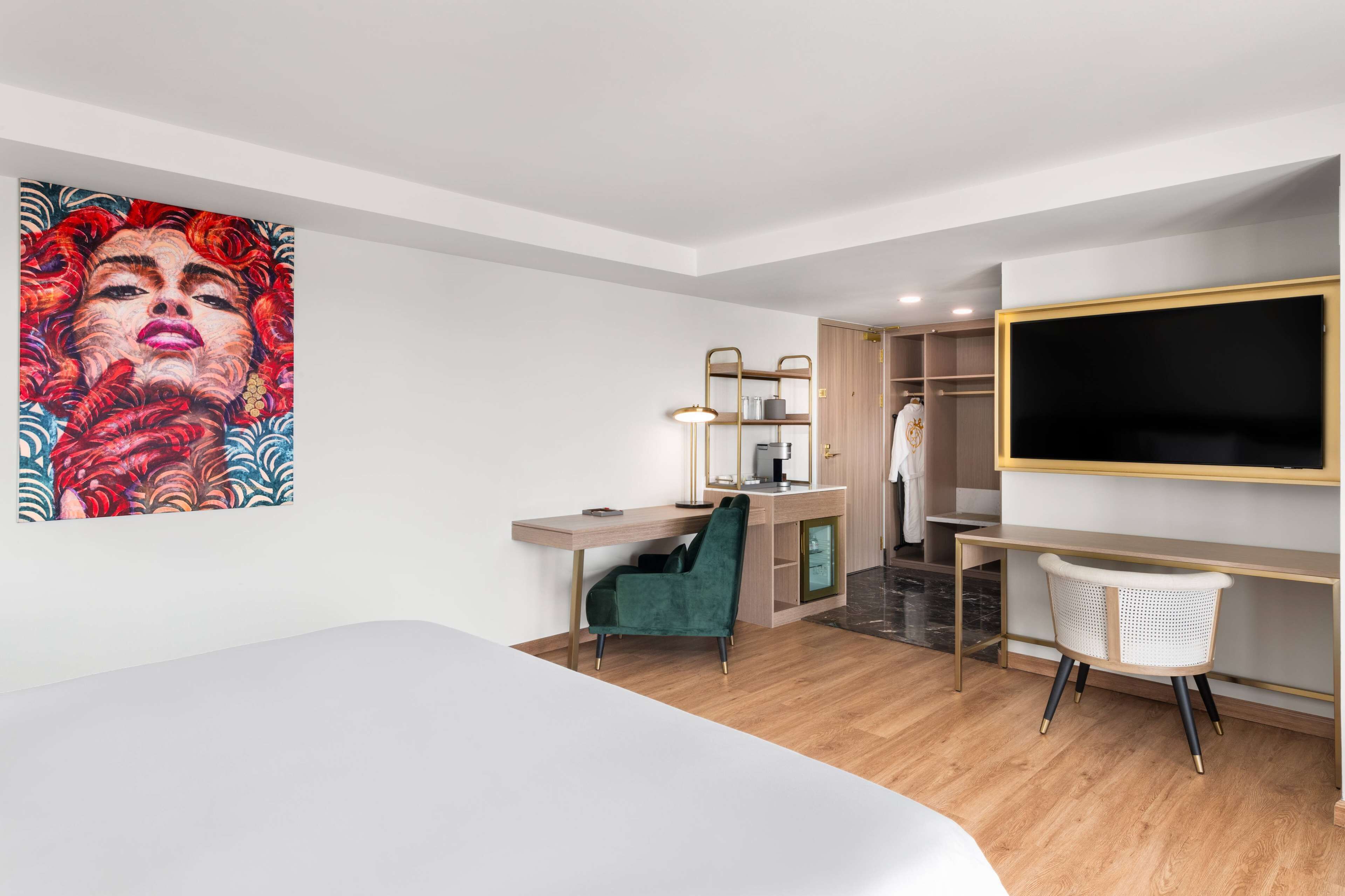 Una habitación de hotel moderna con cama, escritorio, silla, armario y un televisor grande.