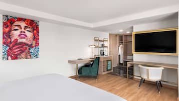 Una habitación de hotel moderna con cama, escritorio, silla, armario y un televisor grande.