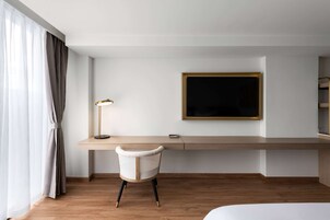 Une chambre d’hôtel avec un bureau en bois, une chaise, un téléviseur fixé au mur et un lit.