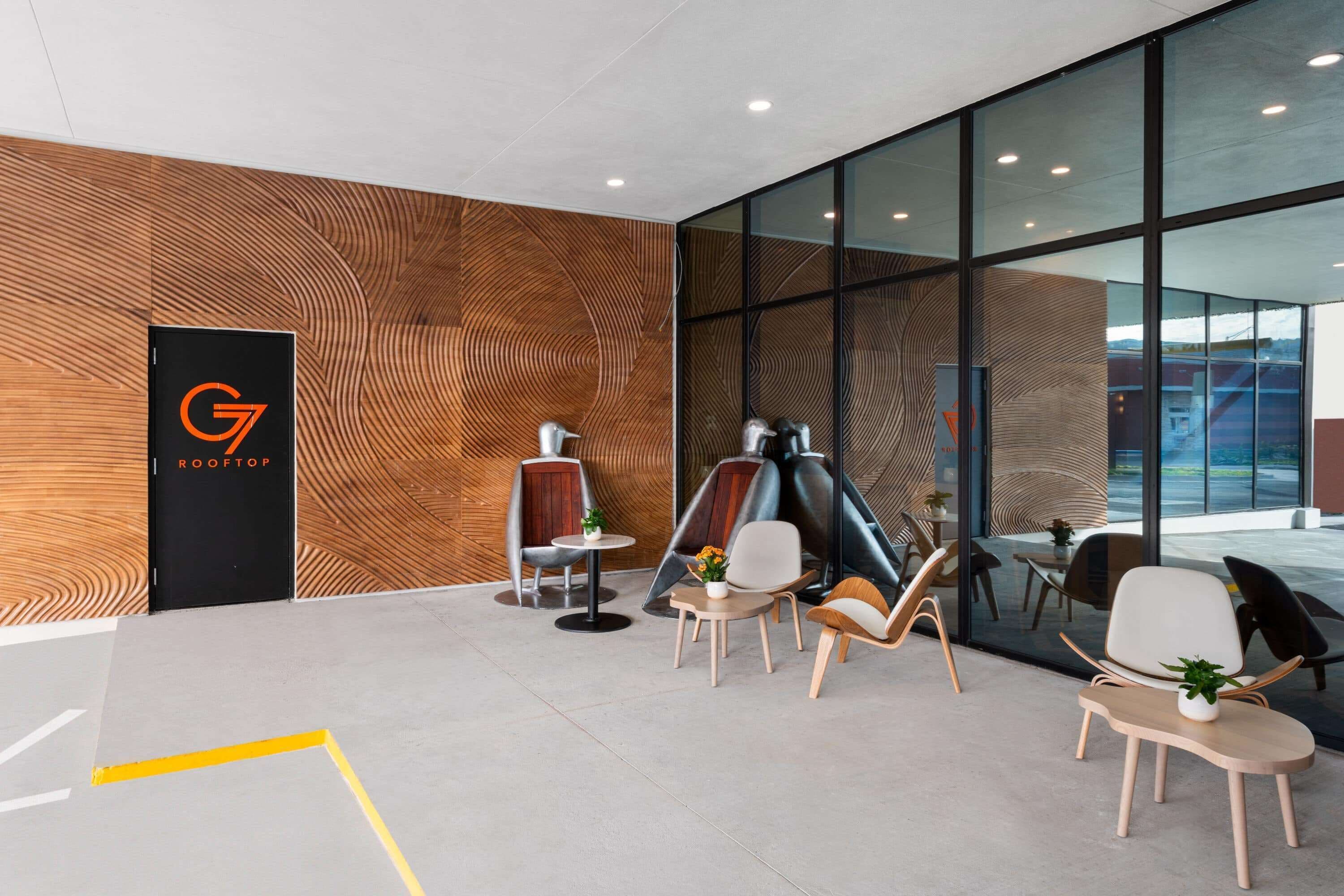 A modern interior with a wooden wall, a black sign with 'G ROOFTOP', and several seating areas with tables and chairs.