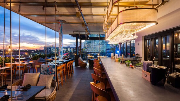 Un espace bar extérieur avec des sièges, une vue sur le paysage urbain et un lustre moderne.