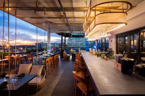 Un área de bar al aire libre con asientos, vistas de la ciudad y una lámpara moderna.