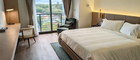 Habitación de hotel con una cama grande, un escritorio con lámpara, una silla, una mesita y vistas al exterior a través de un ventanal.