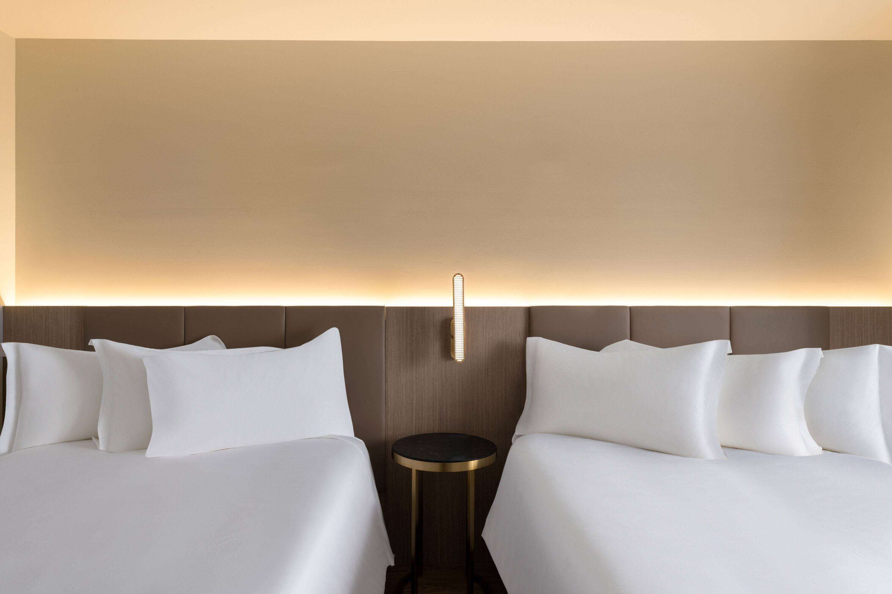 A hotel room with two beds, a round side table, and a wall-mounted light fixture.