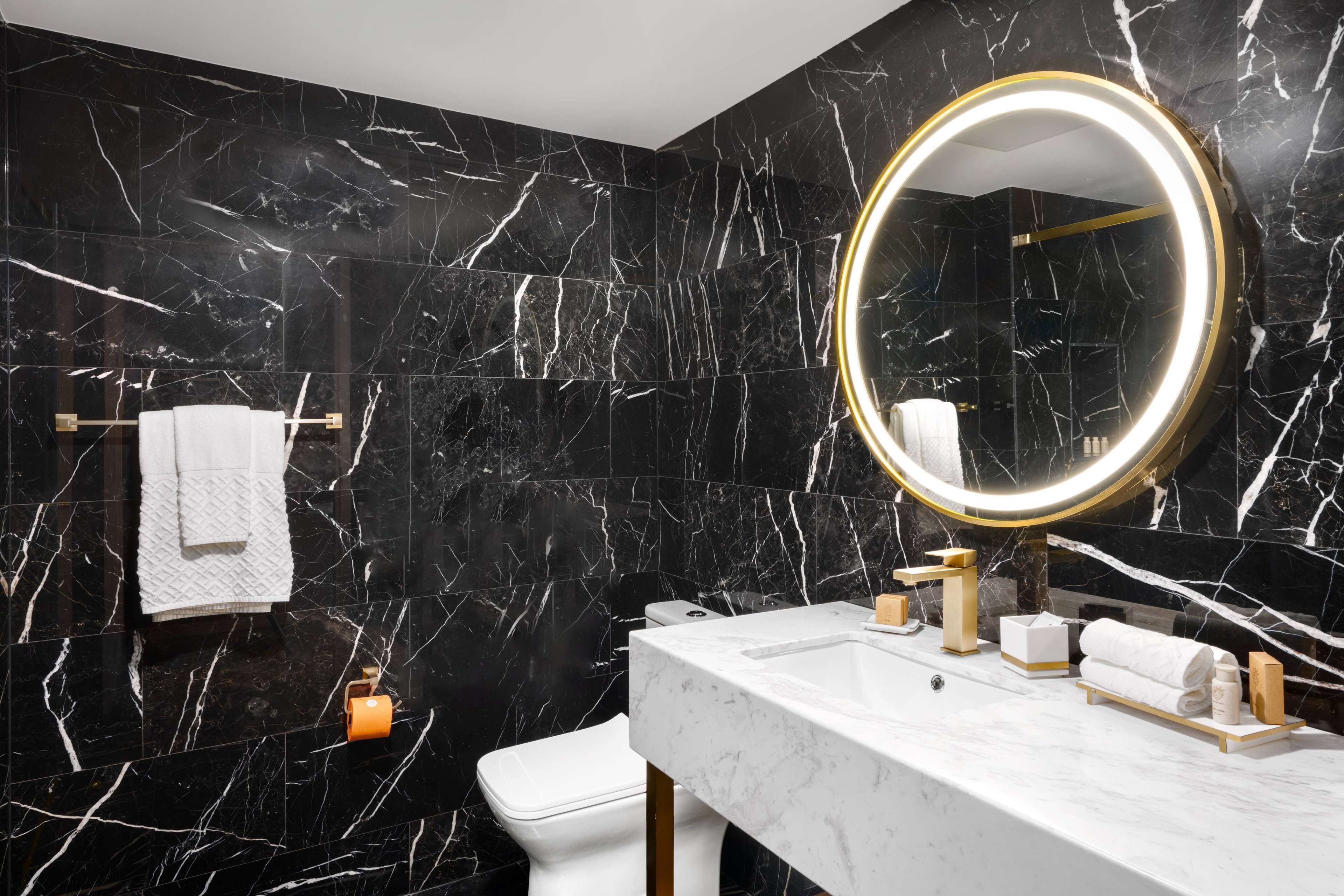 A modern bathroom with black marble walls, a white sink, a gold-framed mirror, and a white toilet.