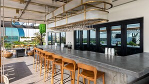 Un espace bar moderne doté d’un long comptoir, de nombreux tabourets et de luminaires suspendus.
