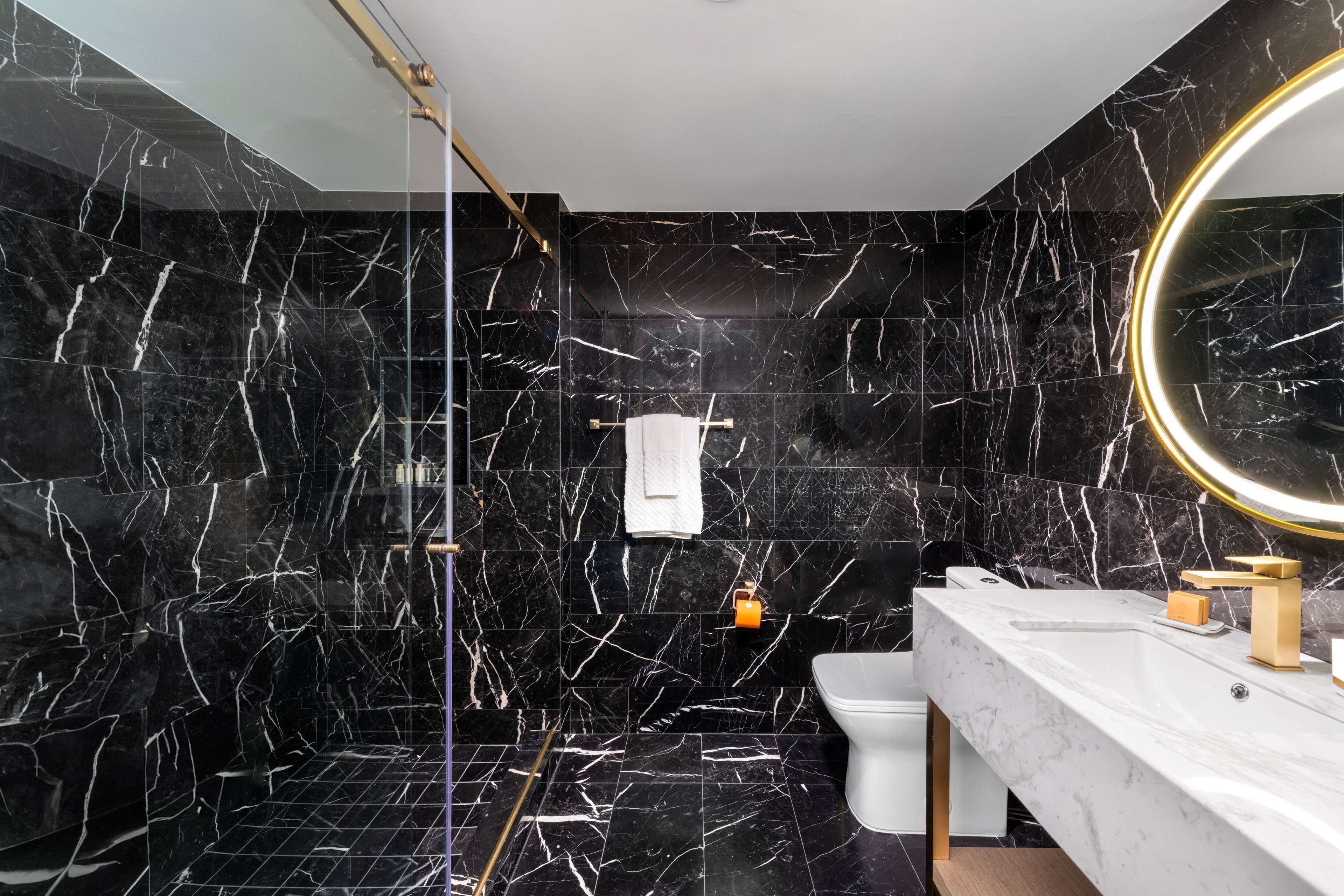 Une salle de bain moderne avec des murs en marbre noir et un lavabo blanc.