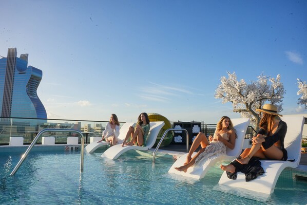 Zona de piscina con sillones de descanso y vista despejada de un edificio moderno al fondo.