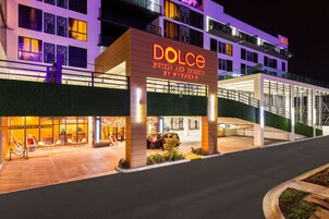 Ein Hotel mit einem gut sichtbaren 'Dolce Hotels and Resorts'-Schild, einem überdachten Eingangsbereich und einem Parkplatz.