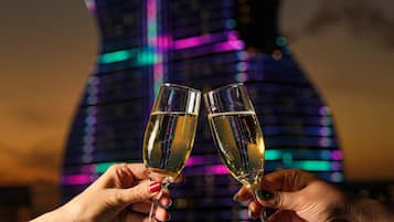 Two hands holding champagne glasses in front of a neon-lit sculpture.