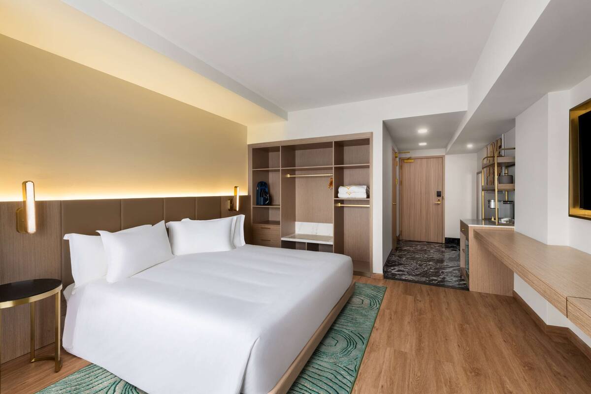 Habitación de hotel con una cama grande, un vestidor, un escritorio con espejo y un televisor montado en la pared.