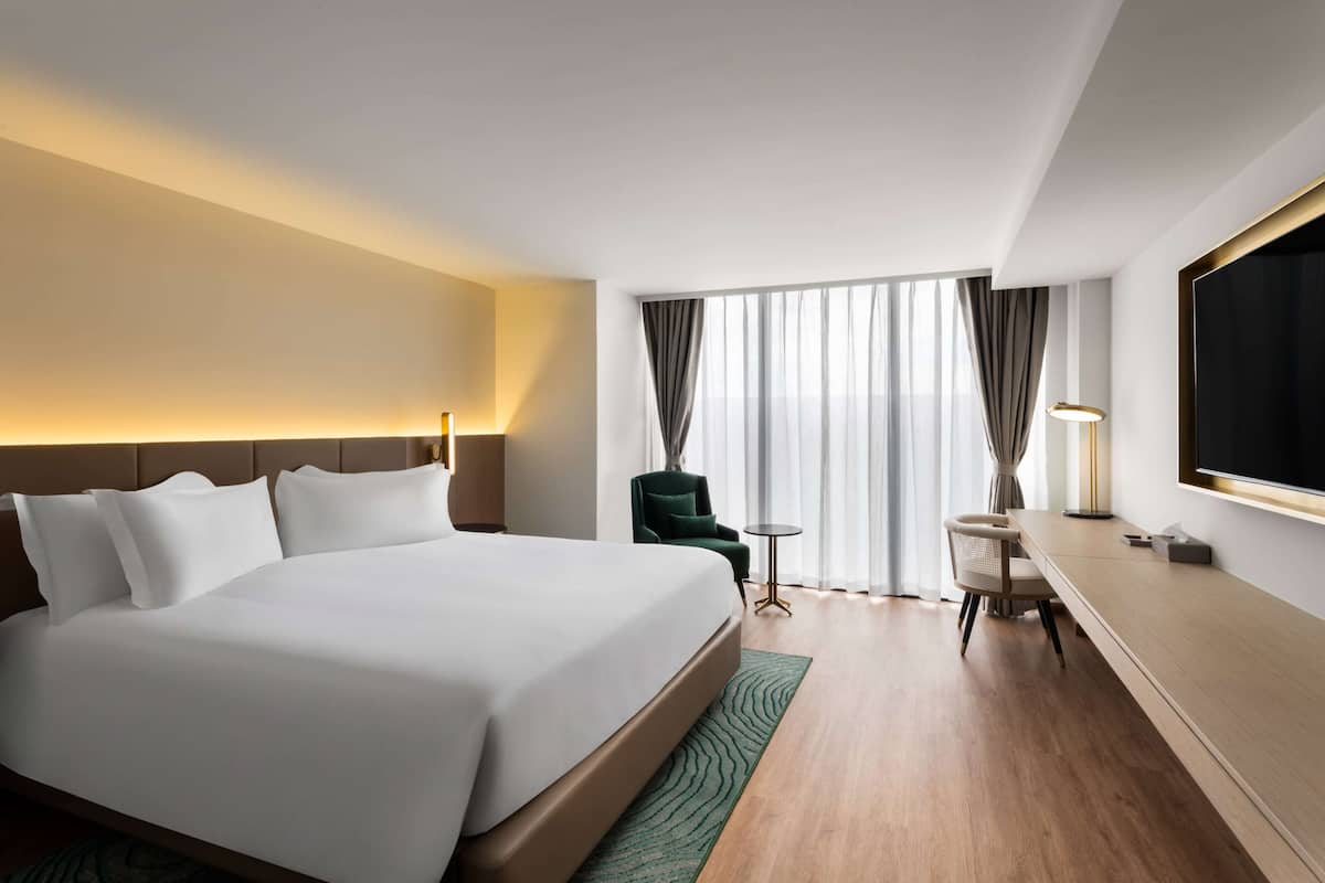 Una habitación de hotel con una cama grande, un escritorio, una silla, un televisor y una ventana con cortinas.