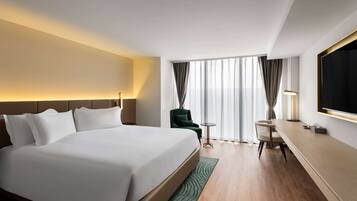 Una habitación de hotel con una cama grande, un escritorio, una silla, un televisor y una ventana con cortinas.