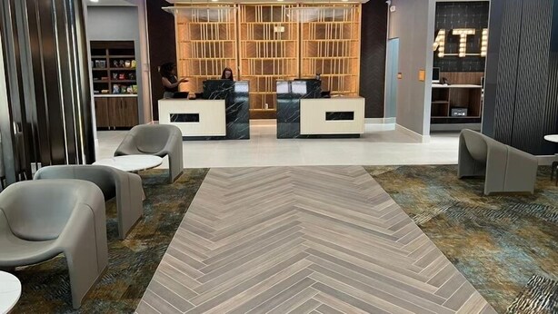 Un área de recepción moderna con alfombra de patrón espiga, dos mostradores de recepción y un separador de madera con diseño de cuadrícula.