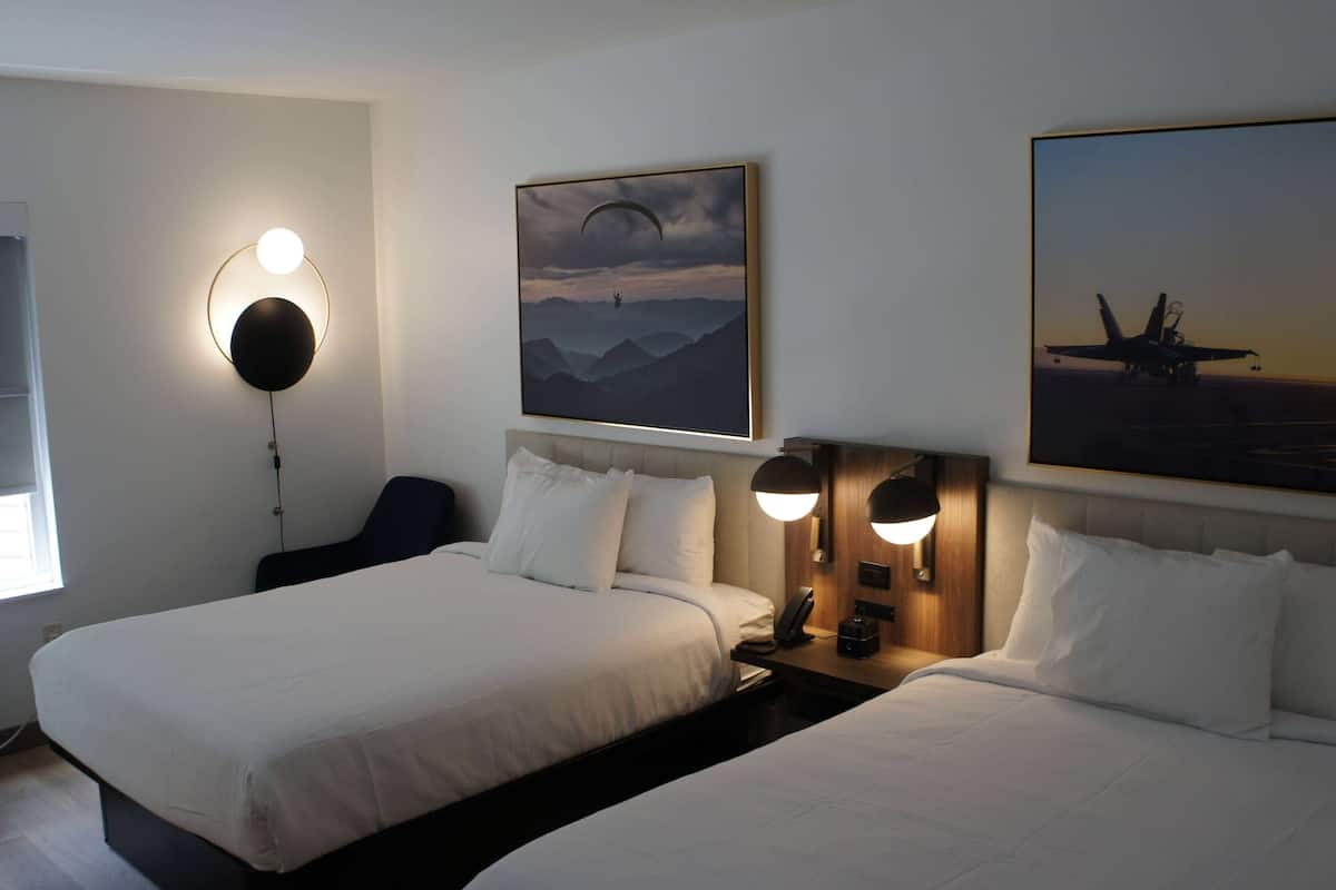 Ein Hotelzimmer mit zwei Betten, einem Nachttisch mit Lampen und zwei gerahmten Bildern an der Wand.