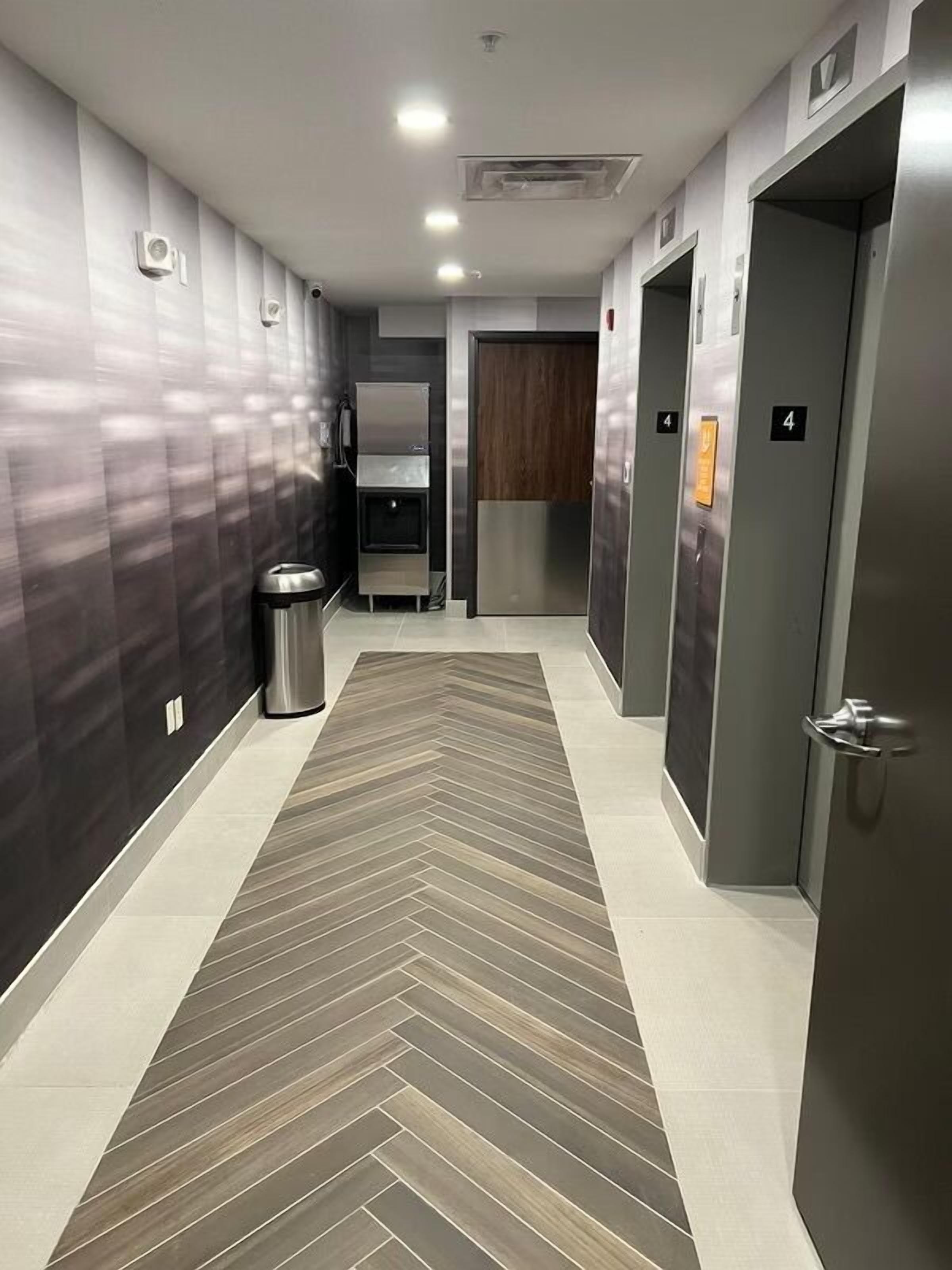 A modern hallway with a herringbone-patterned floor, metallic lockers, and a trash bin.
