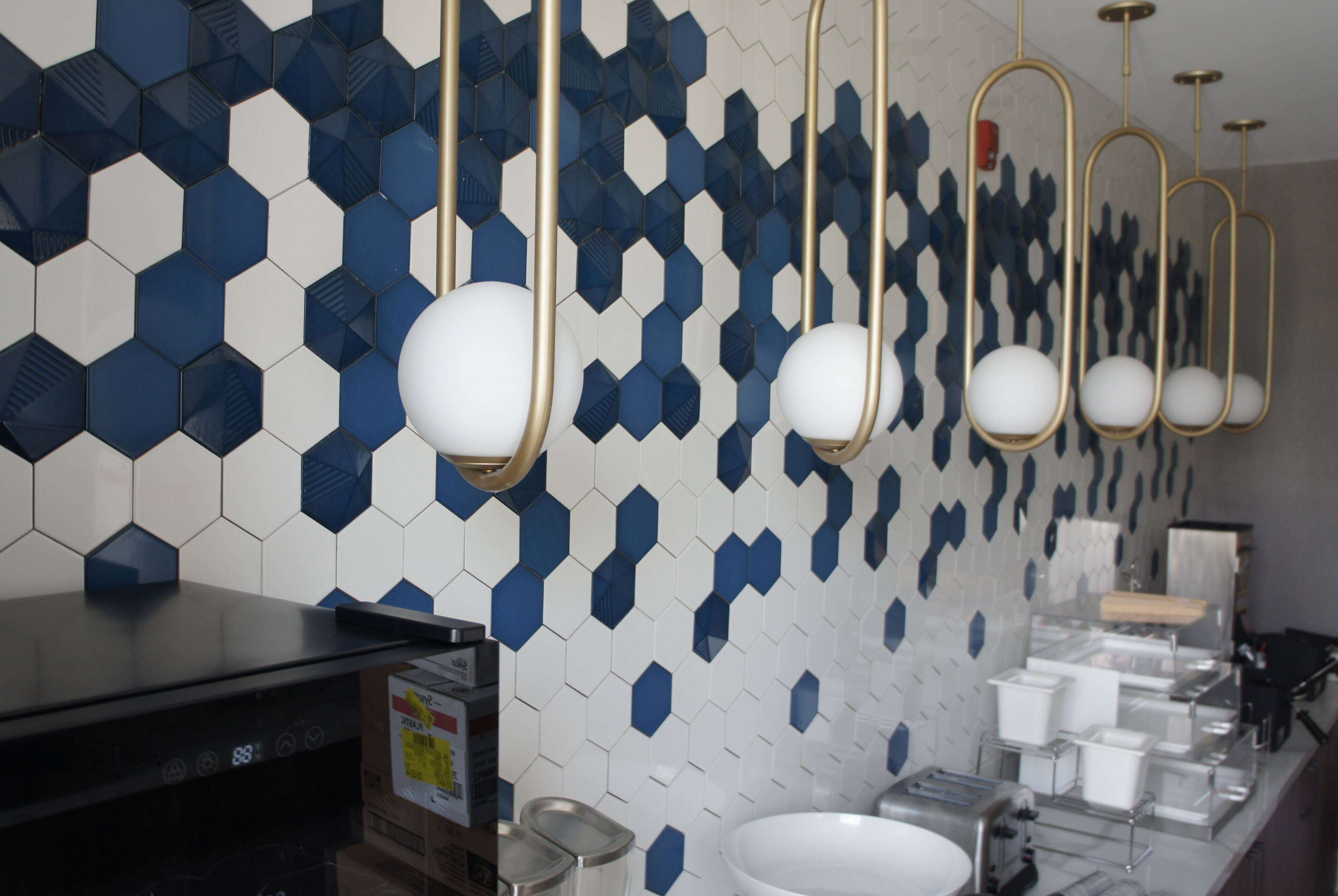A modern bathroom with a hexagonal tile backsplash, a black countertop, a sink, and a mirror.