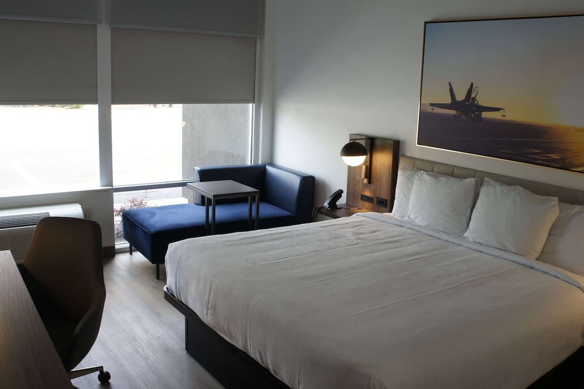 Ein Hotelzimmer mit einem großen Bett, einem Schreibtisch, einem Stuhl, einem kleinen Tisch und einem Fenster mit Blick auf ein am Boden stehendes Flugzeug.