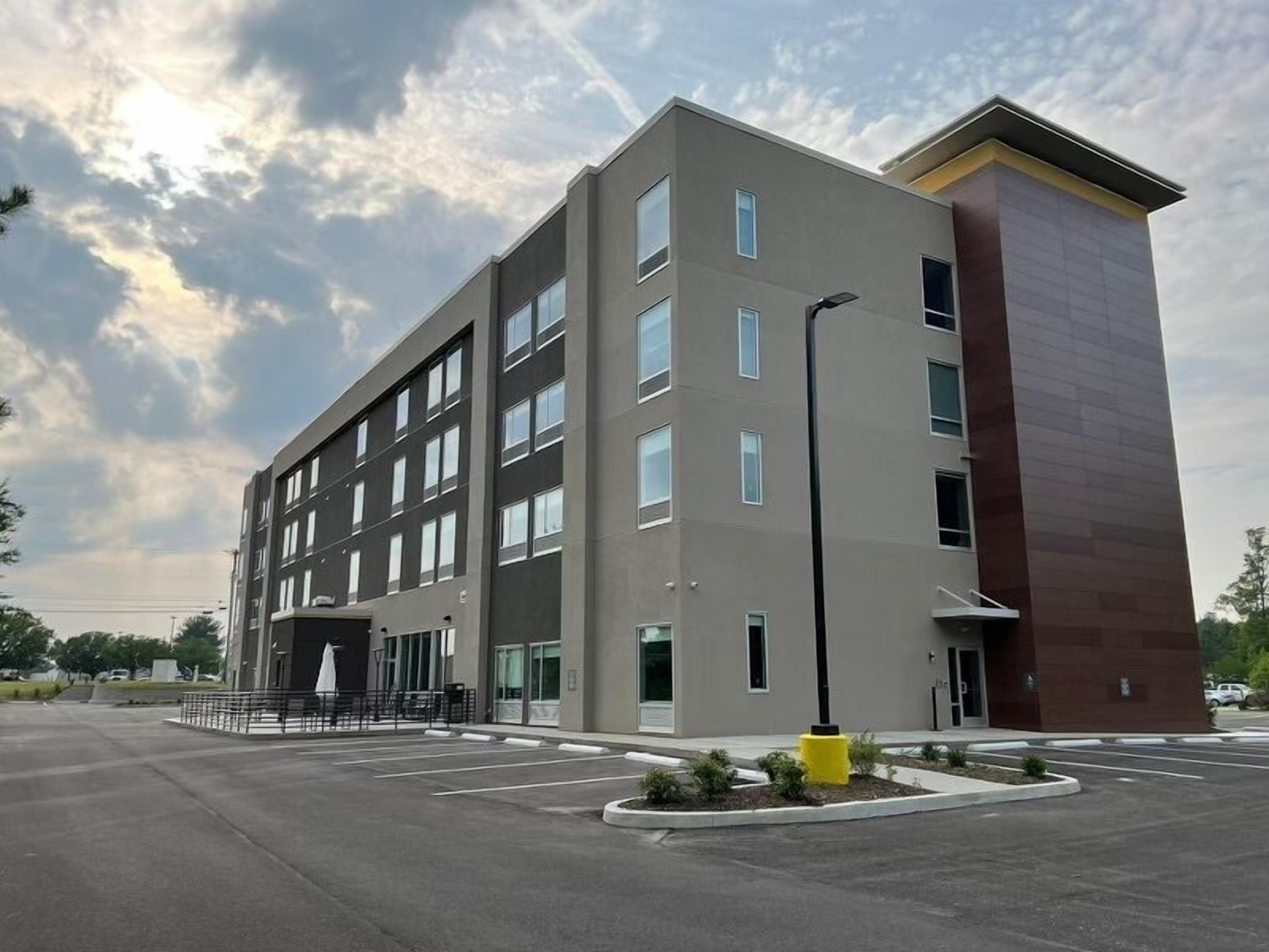 A multi-story building with a flat roof, large windows, and a parking lot in front.