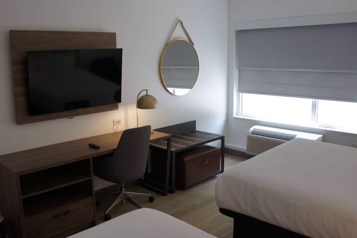 Ein Hotelzimmer mit Fernseher, Schreibtisch, Stuhl und zwei Betten.