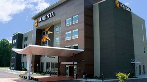Un hotel moderno con un llamativo letrero de 'La Quinta', una entrada cubierta y un cielo despejado.