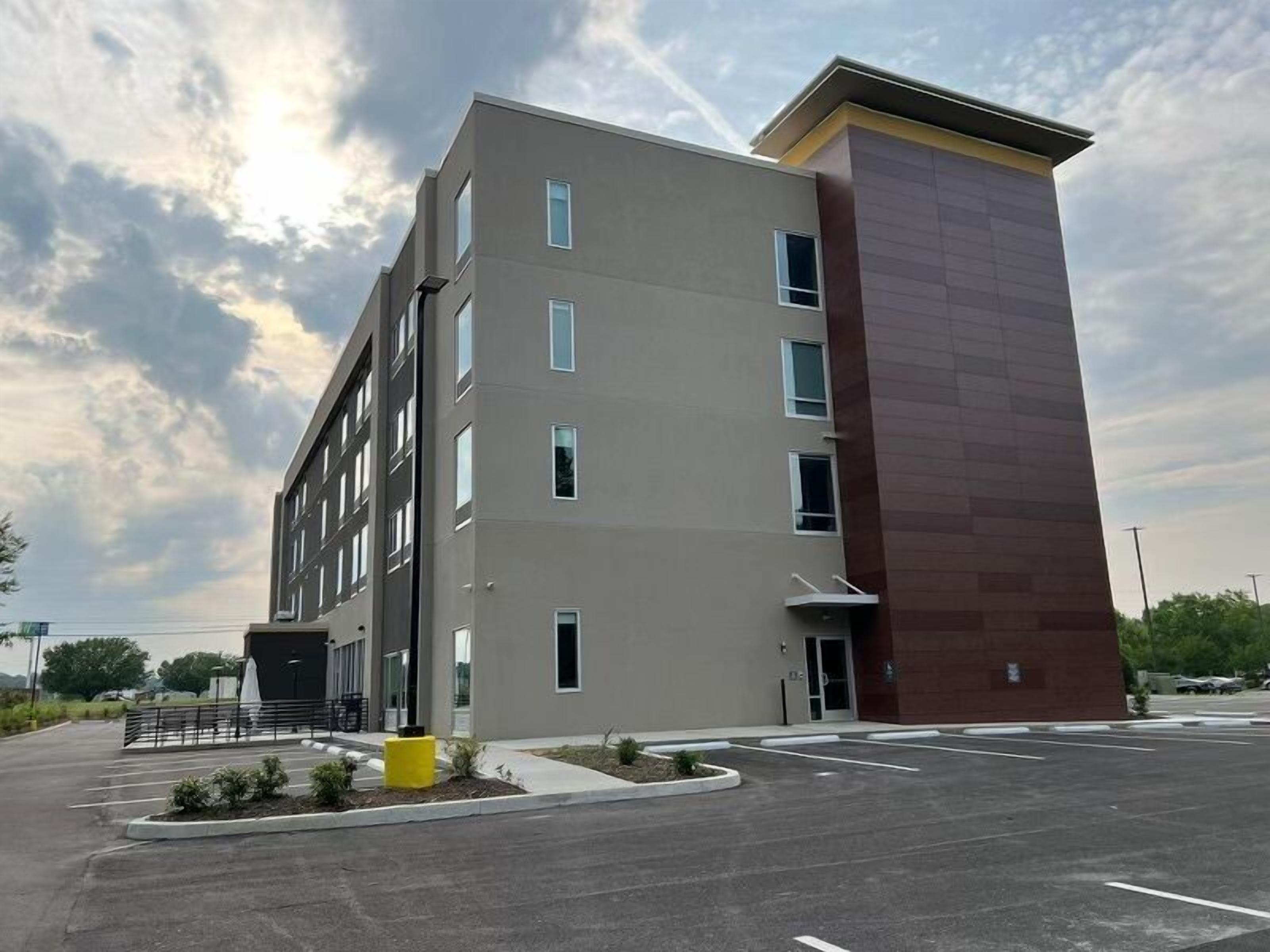 A multi-story building with a flat facade, a parking lot in front, and a clear sky.
