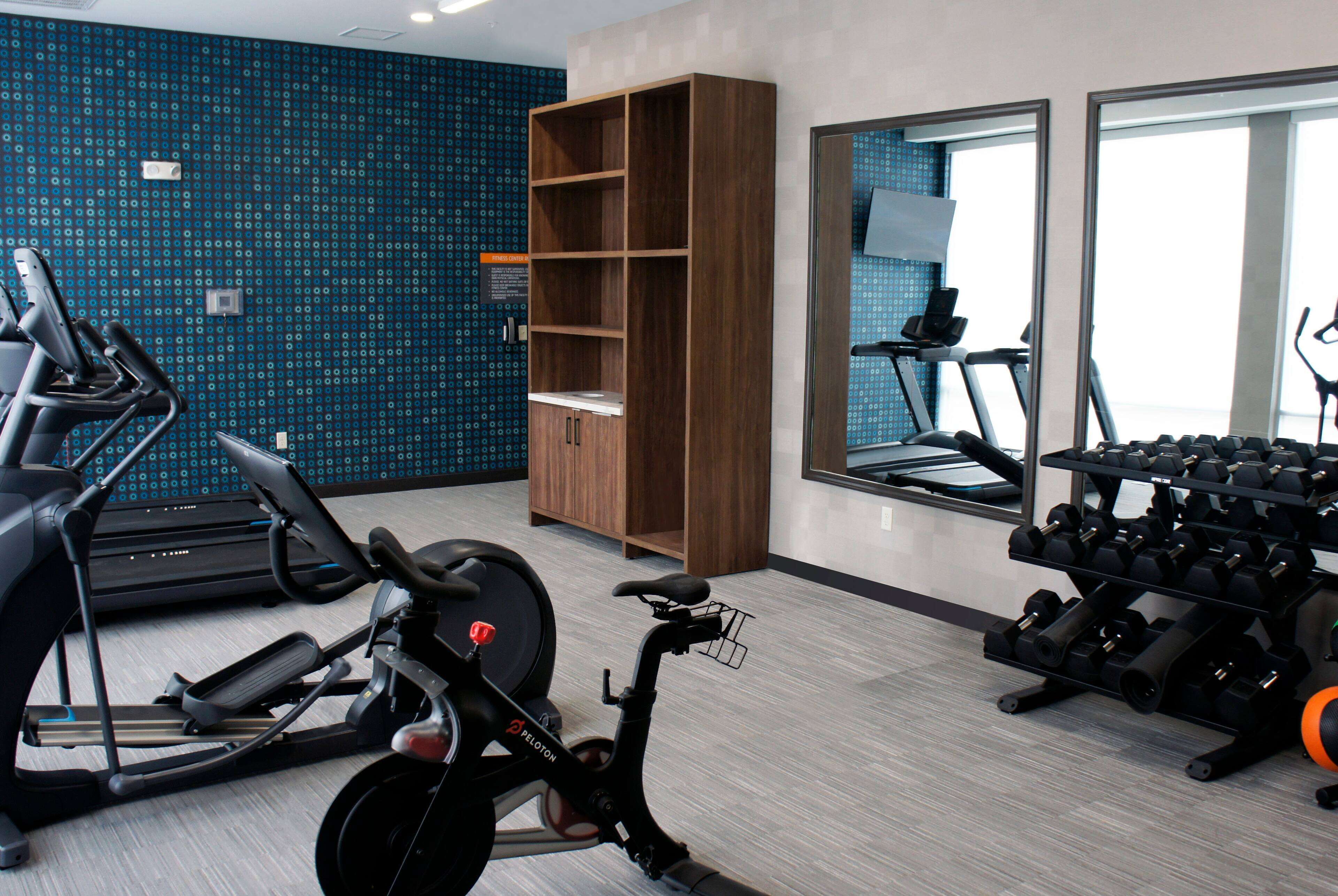 A gym with exercise equipment, a mirrored wall, and a blue patterned wall.