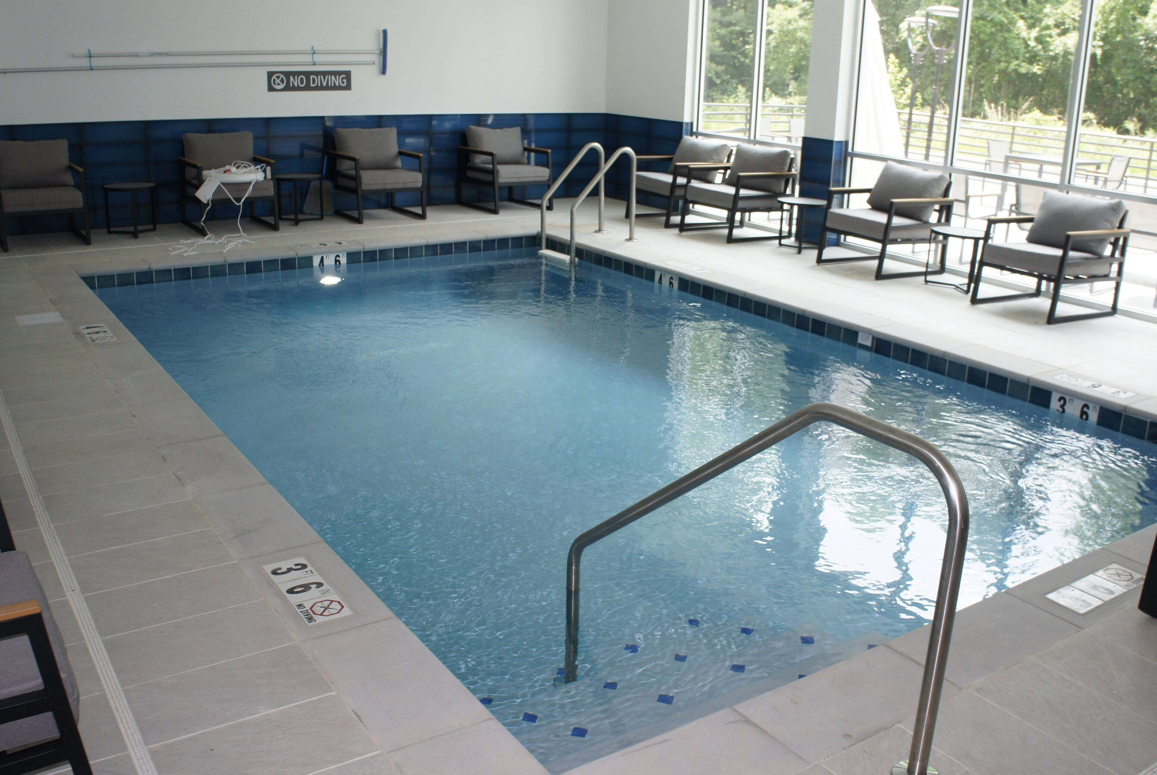 An indoor swimming pool with a 'No Diving' sign, lounge chairs, and a clear view of the outdoors through large windows.
