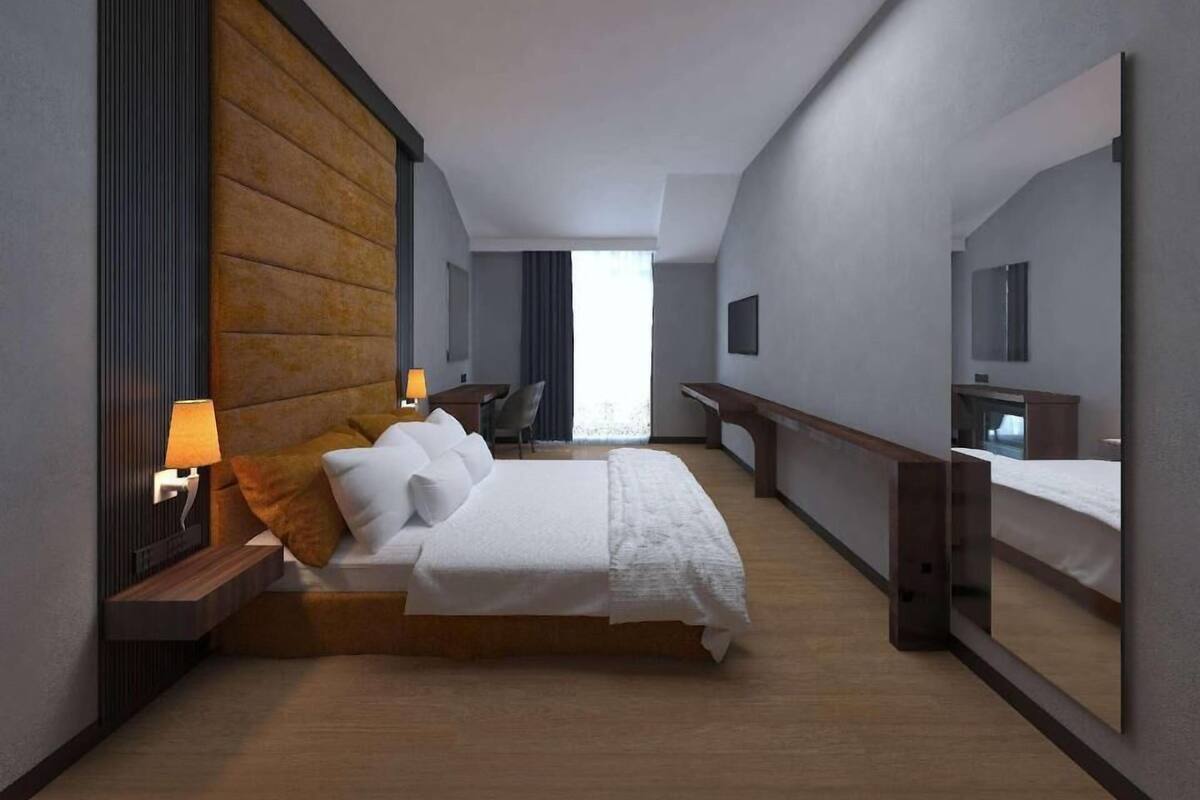 Una habitación de hotel moderna con una cama grande, un escritorio, una silla, un televisor y un espejo amplio.