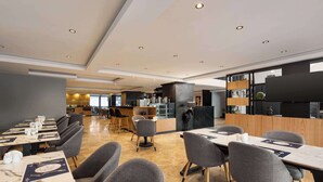Un restaurante moderno con mesas de mármol, sillas tapizadas en gris y una zona de bar central.