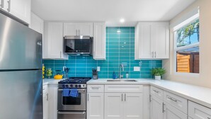 A modern kitchen with white cabinets, a stainless steel refrigerator, a gas stove, and a microwave. - Pet-Friendly OB Bungalow w/ Patio, Grill & Walk to Beach (San Diego)