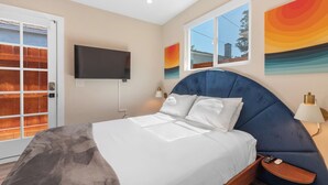 A modern bedroom with a large bed, a TV mounted on the wall, and a window with a view of the outside. - Pet-Friendly OB Bungalow w/ Patio, Grill & Walk to Beach (San Diego)