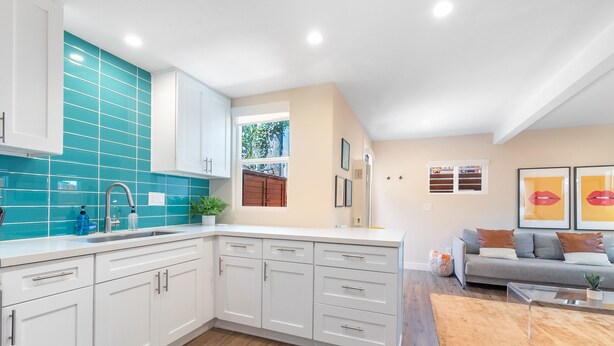 A modern kitchen with white cabinets, teal backsplash, and wooden flooring. - Pet-Friendly OB Bungalow w/ Patio, Grill & Walk to Beach (San Diego)